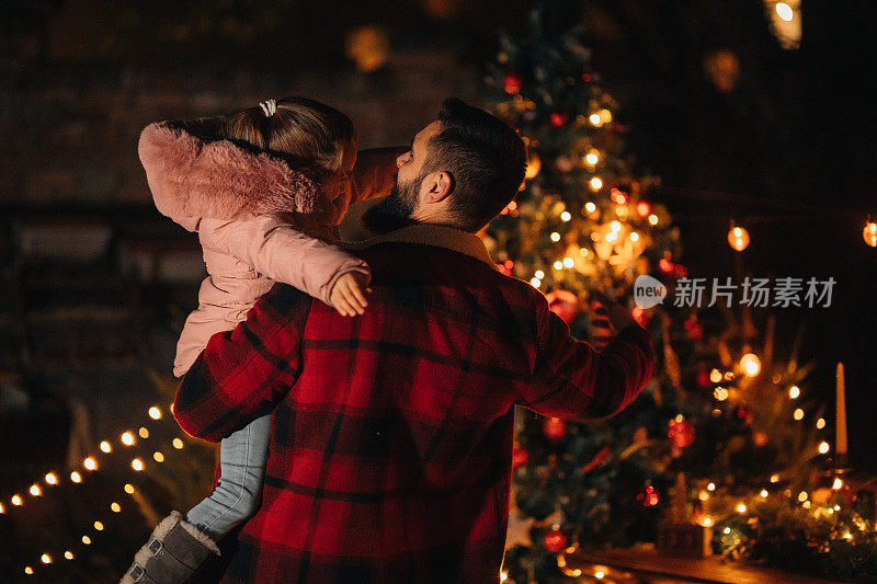 年轻的父亲抱着他的小女儿在圣诞树前