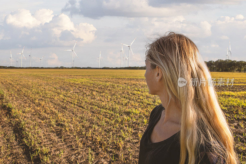 田里的女农民望向远方，风力涡轮机在远处