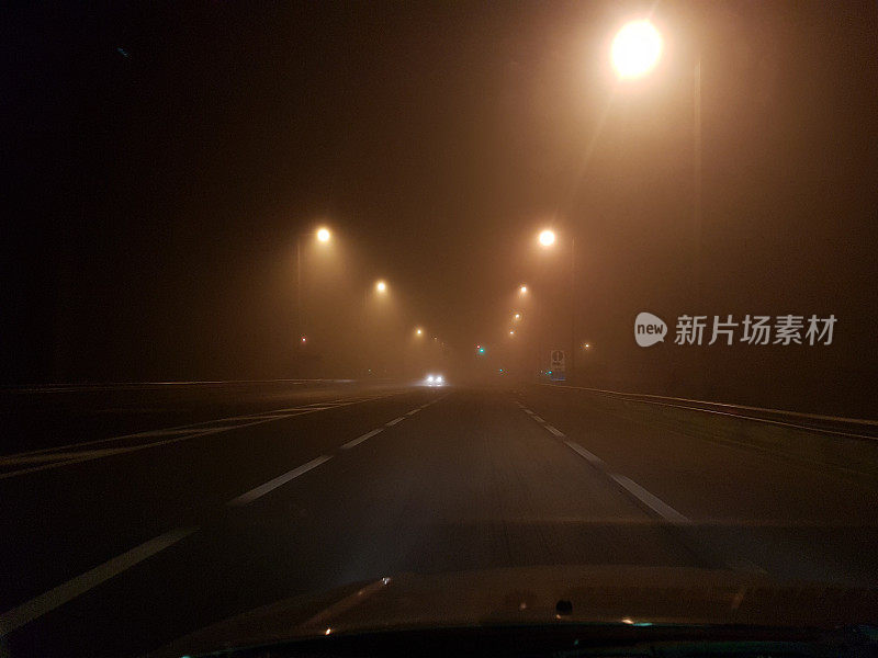 在大雾弥漫的夜晚，希腊埃格纳蒂亚大街上的道路车辆亮起了灯