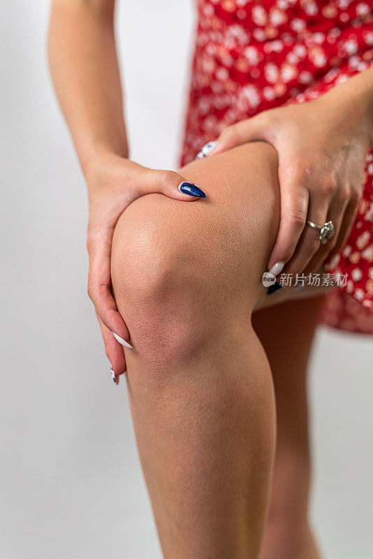 穿着裙子的膝盖疼痛的年轻女孩抱着她疼痛的膝盖。膝盖和关节疼痛。