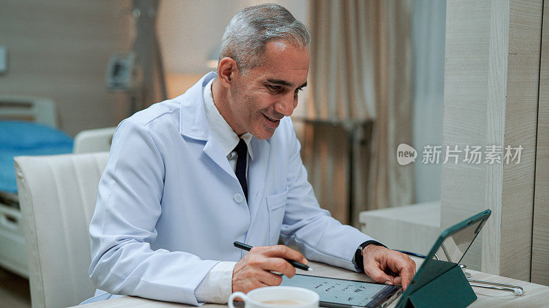 成年男性医生在与客户视频会议期间在记事本上记录笔记。