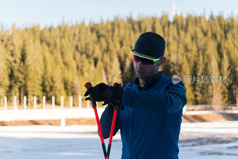 帅气的男运动员越野滑雪板，呼吸新鲜空气，在雪林艰苦训练后休息。检查smartwatch。健康的冬季生活方式。