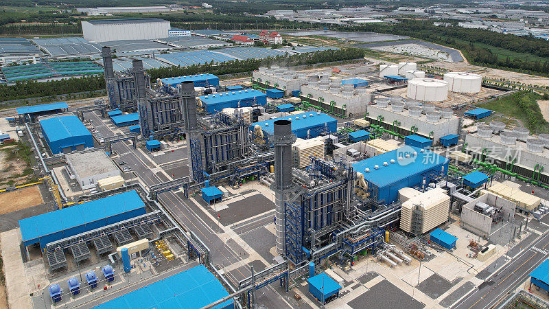 电厂鸟瞰图，以及工业厂区内的炼油厂储油罐。安装在工业建筑屋顶上生产绿色生态电力的蓝色屋顶电厂鸟瞰图。生产的可持续