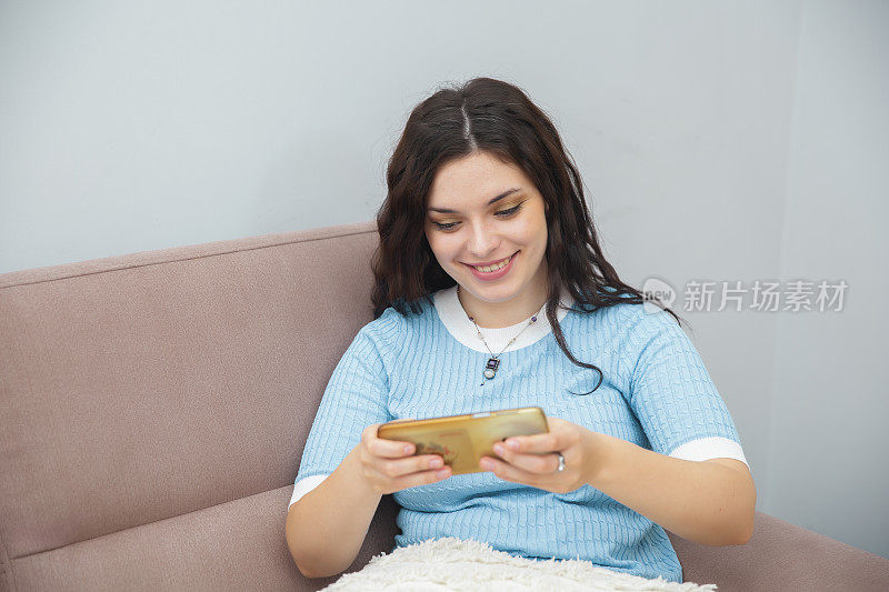 女人坐在沙发上，玩着手机，面带微笑