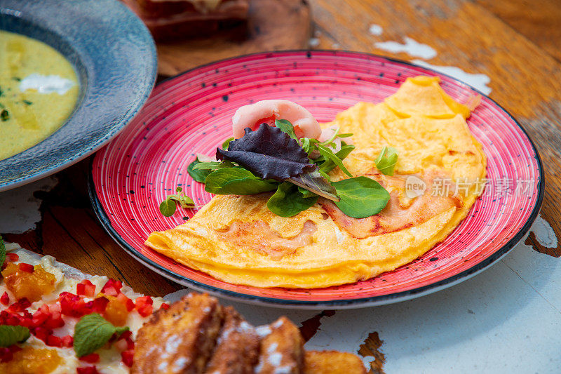 折叠的煎蛋卷与火腿片和香草叶一起放在木桌上与其他餐点