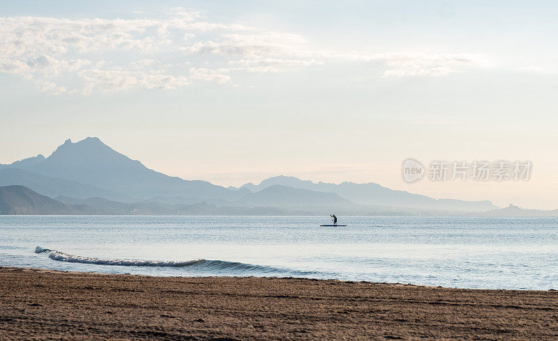 清晨的海景、山脉和海岸线。广阔的蓝色大海和背景中的两个人在充气冲浪板上。