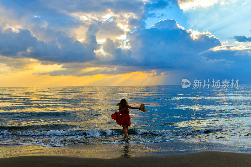 日落漫步在沙滩上。日落时分，年轻女子在海边玩耍。