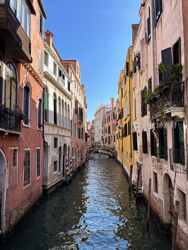 红色和白色条纹系泊杆在狭窄的运河，威尼斯，意大利，横跨桥，清澈的蓝色晴朗的天空，小缩小的视角，重点在前景
