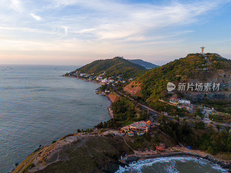 从上面俯瞰云头海岸全景，海浪、海岸线、街道、椰子树、越南Nho山后面的基督国王雕像