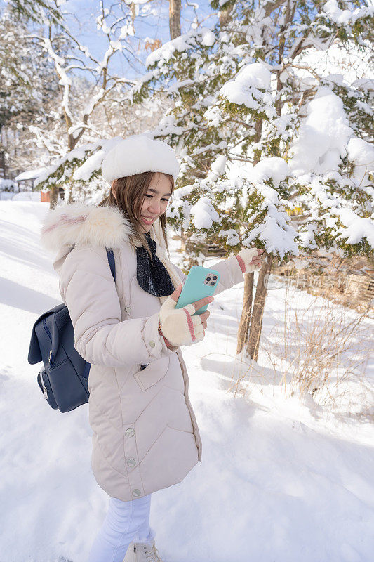 美丽的女游客用电话享受她的日本之旅在雪的冬天