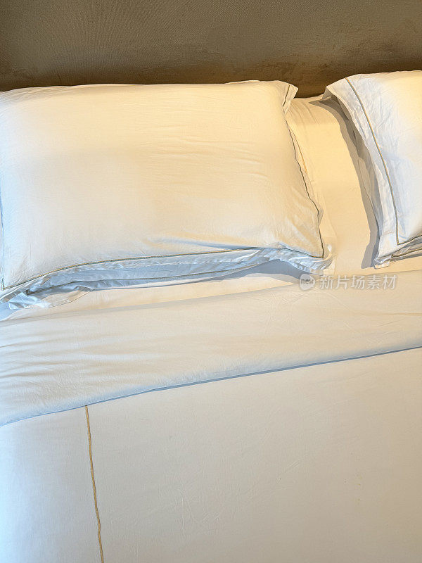 白色羽绒被覆盖的双人床，堆叠的白色酒店枕头，折痕床上用品，麂皮效果床头板，抬高的视野