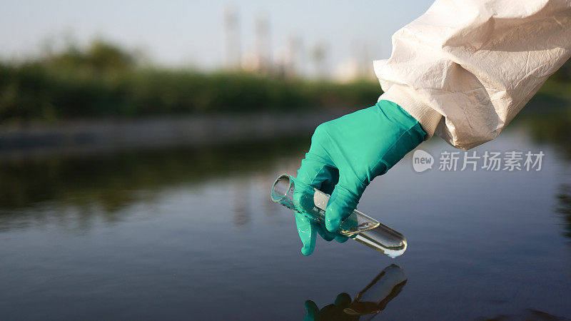 特写科学家或环境工程师的手，穿着化学防护服和个人防护装备，从工业的化学烧瓶中收集有毒废水样本