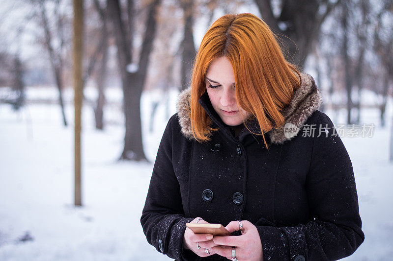 美丽的姜黄色女孩在雪地里拿着手机。