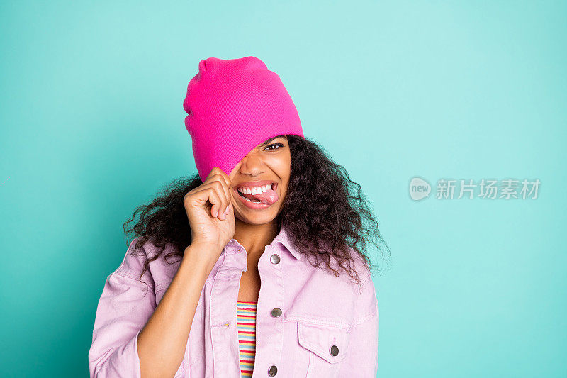照片上的快乐不礼貌粗鲁的女孩伸出她的舌头在条纹t恤夹克粉红色显示拉她的帽子在她的头上孤立的生动的蓝绿色背景
