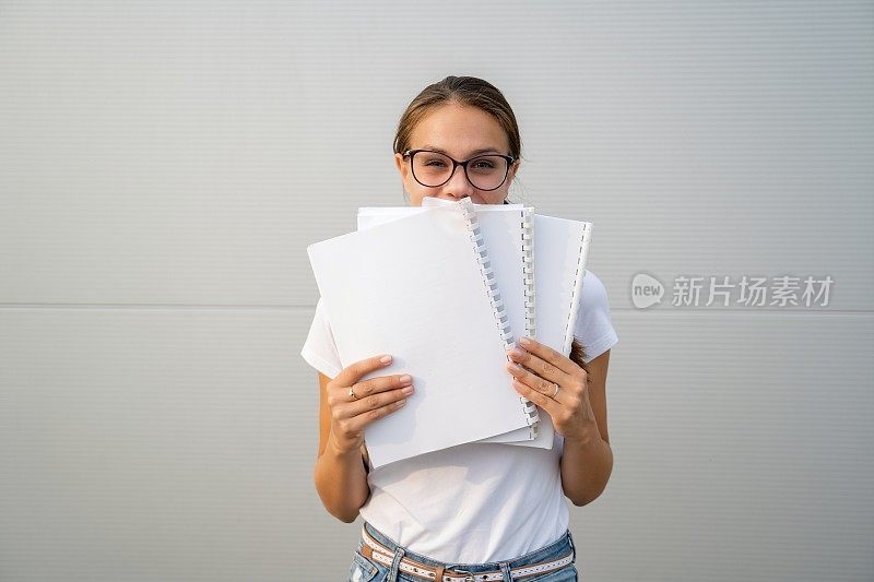 年轻的女学生展示她的新笔记本和隐藏一半她的脸与他们-股票照片