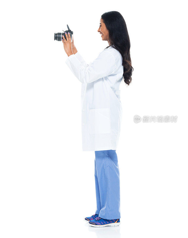 拉丁美洲和西班牙裔的年轻女性游客站在白色背景穿着实验室大褂，拿着相机