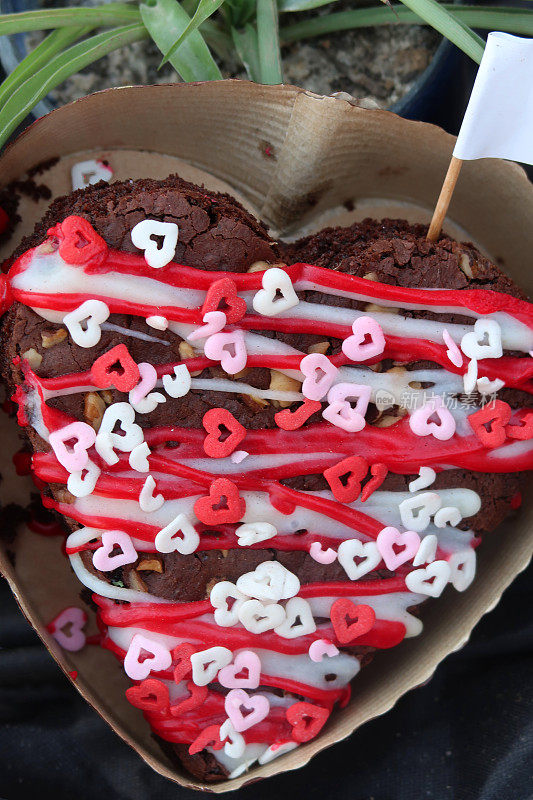 巧克力布朗尼蛋糕切成心形，上面有坚果、红白糖霜和心形糖果