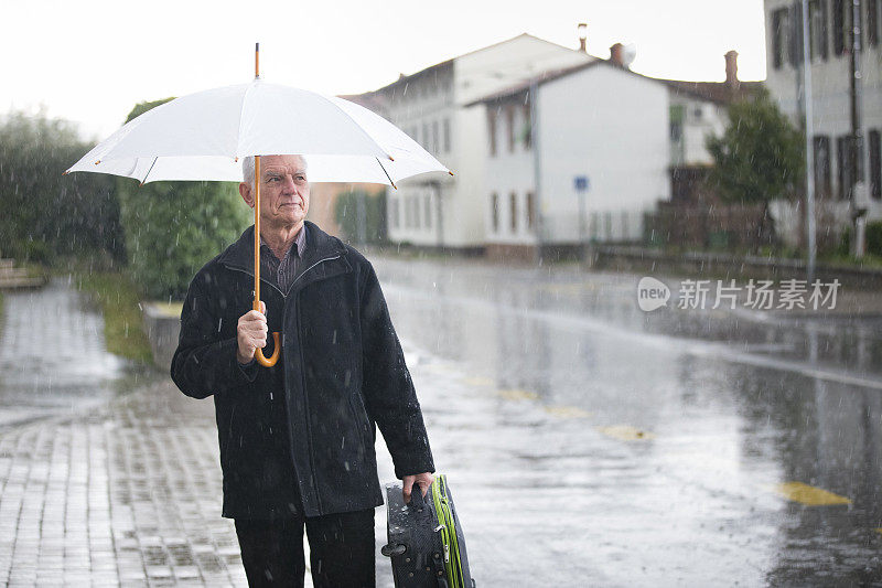 一位老人撑着伞站在雨中的人行道上