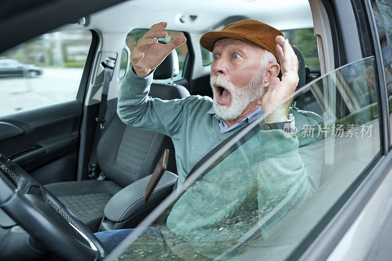 一名戴着帽子的老人坐在车里开车，意外地把智能手机掉在地上，因鲁莽驾驶而发生车祸