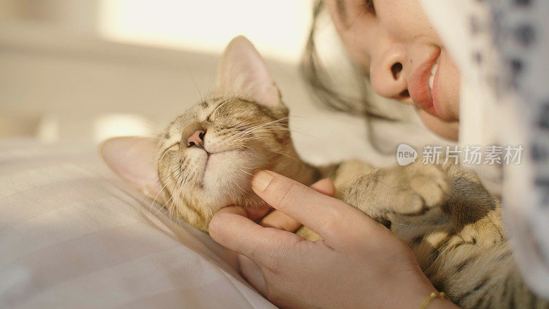 一位年轻女子在卧室白色的床上抚摸她的猫。