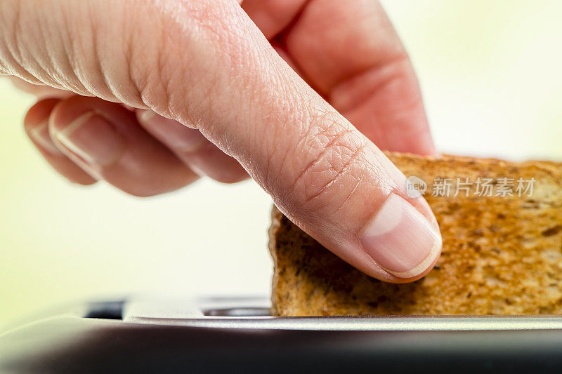 Hand正在从烤面包机中取出新鲜酥脆的烤面包
