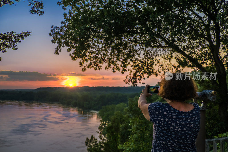 在河边拍摄日落的女人