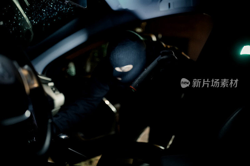 穿着黑色巴拉克拉瓦帽的偷车贼试图用螺丝刀闯入汽车。偷车贼，偷车贼