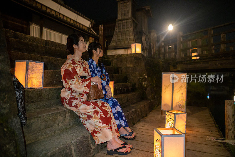 母亲和女儿在浴田坐在台阶上看纸灯笼在传统的日本牛郎长崎节