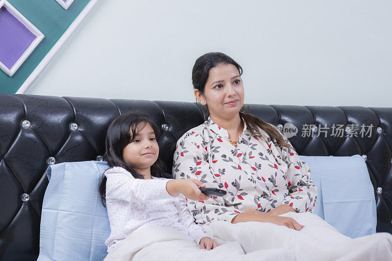 年轻的妈妈和可爱的小女儿在床上看电视，库存照片