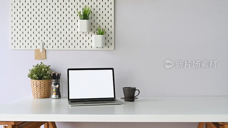 一个白色的空白屏幕的电脑笔记本电脑正在一个白色的工作空间周围的办公设备。