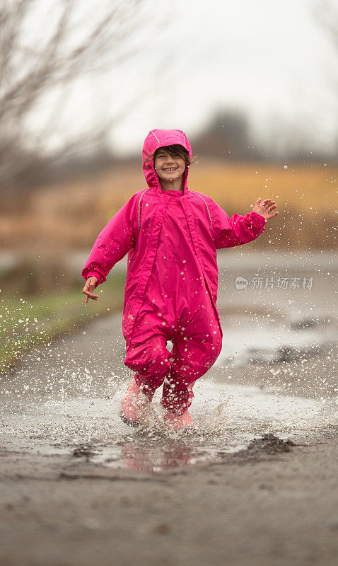 女孩跑过雨水坑在粉红色的雨衣