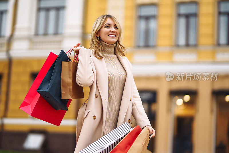年轻女子穿着一件薄外套，微笑着，在她的手中拿着五颜六色的购物袋。