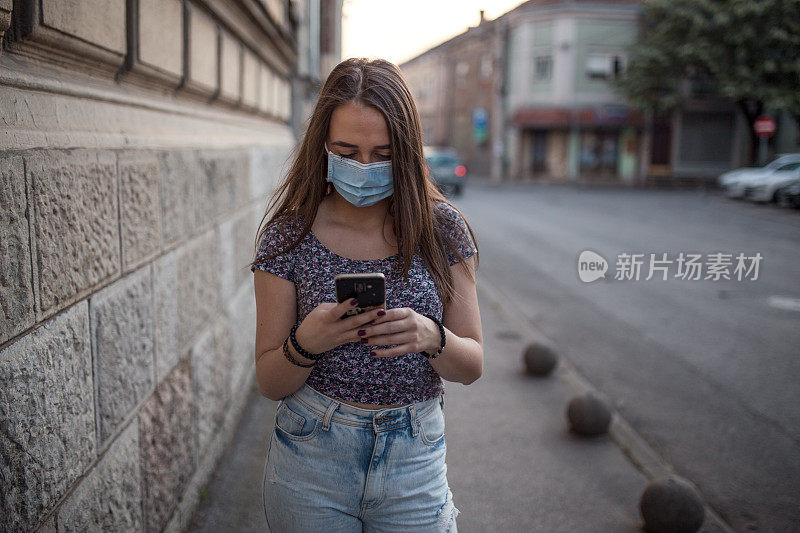 一名年轻女子戴着防护面具在街上使用手机