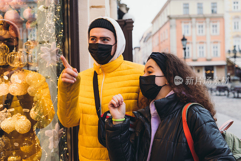 年轻夫妇戴着面具从购物窗口中挑选完美的圣诞礼物