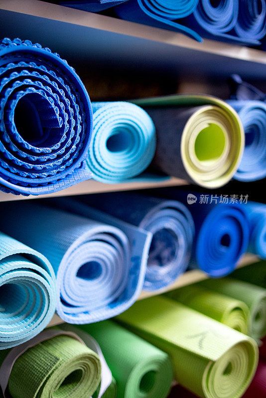 在健身房仓库的架子上有蓝色和绿色的运动垫