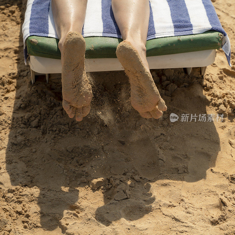 一个成熟女人的脚在热带海滩的躺椅上休息。