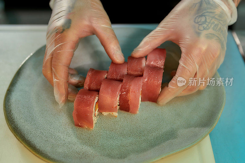 在商业厨房准备卷时，厨师将金枪鱼寿司切片放在盘子上的手的特写