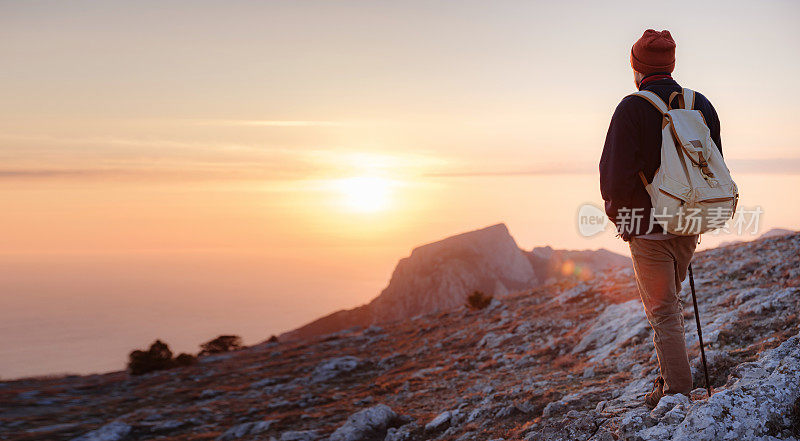 夕阳西下时，一名男子站在山崖顶上，欣赏大自然的美景