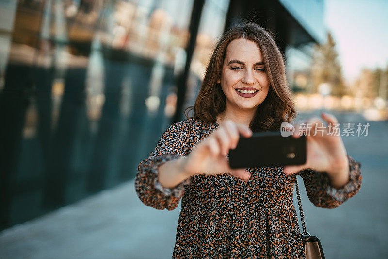 微笑的女人在城市的街道上用智能手机自拍