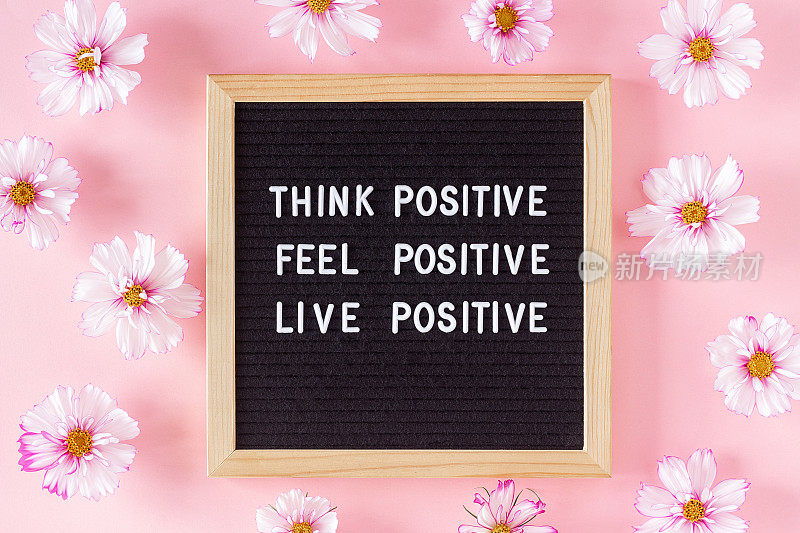 积极地思考，积极地感受，积极地生活。在信笺板和粉红色背景上的鲜花激励的引用。这是一天中鼓舞人心的概念。平铺视图
