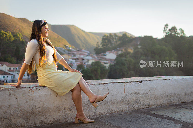 年轻的女旅行者坐在一座历史悠久的桥上欣赏日落。