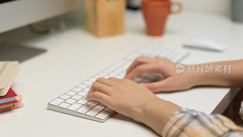 女自由职业者双手敲击电脑键盘上的白色桌子上的办公用品