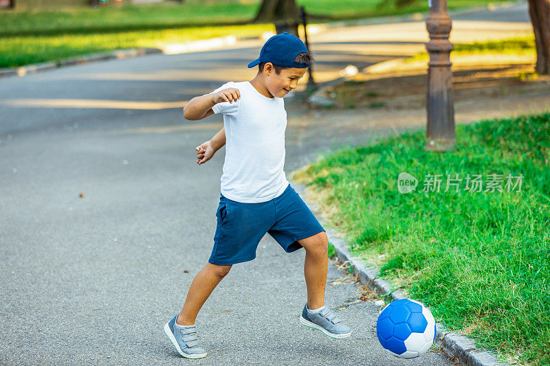 一个可爱的小男孩在夏天的公园踢足球。