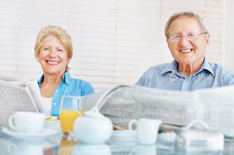 一对幸福的老夫妇在早餐桌上读报纸