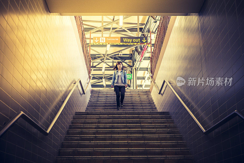 一位年轻的亚洲女子在阳光下走下火车站的台阶