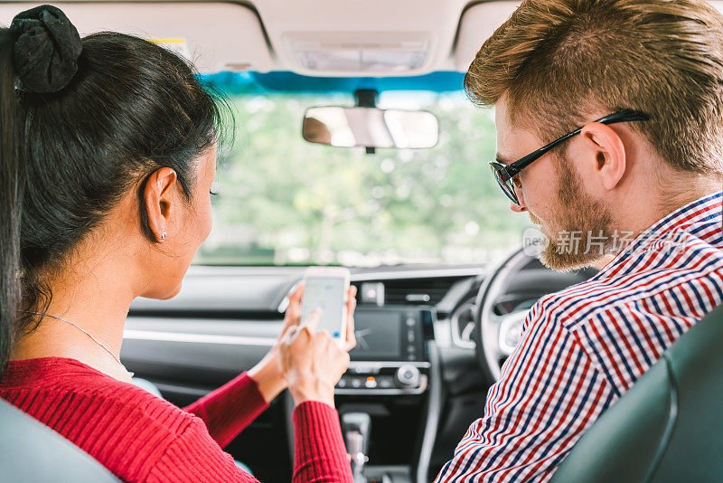 多民族情侣，白人男子和黑人亚洲女孩使用智能手机上的导航系统应用程序在车。现代小工具的生活方式，家庭旅行活动，或在线出租车呼叫请求服务概念。