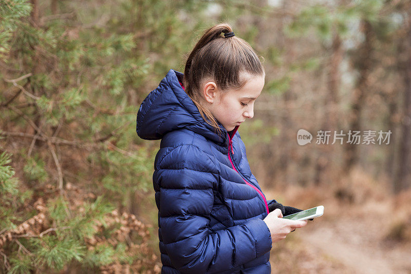 可爱的女孩在树林里玩手机