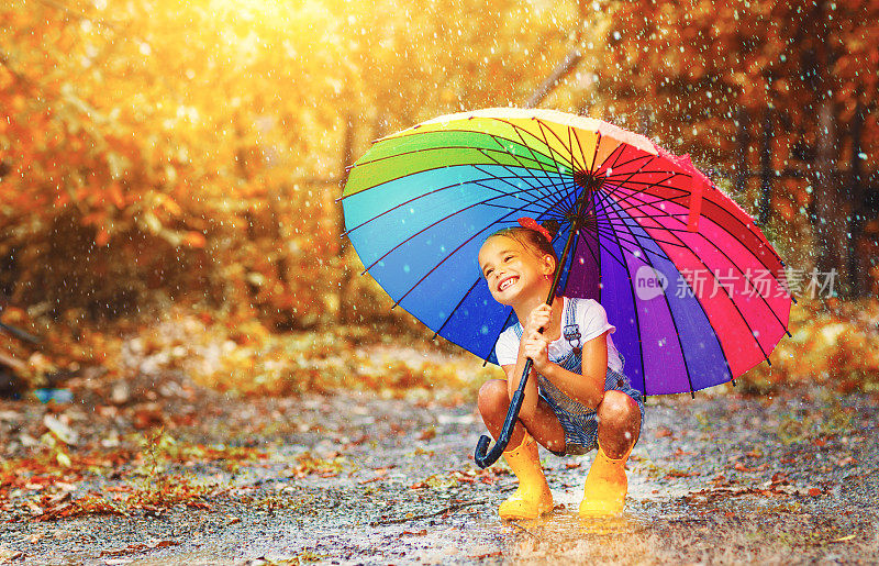 快乐有趣的孩子女孩与伞跳在水坑在橡胶靴子