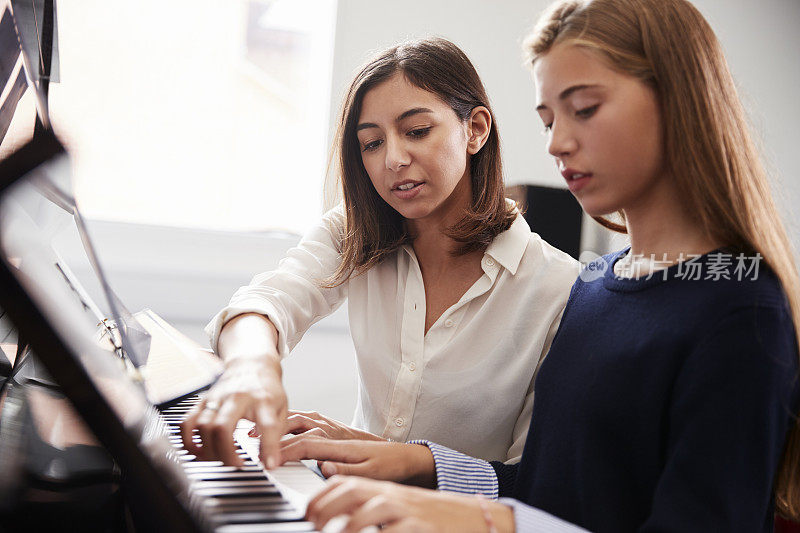 在音乐课上，女学生与老师一起弹钢琴