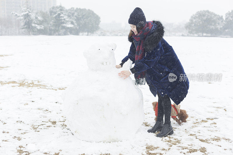 一个快乐的女人和她的狗在雪地上堆了一个大雪人